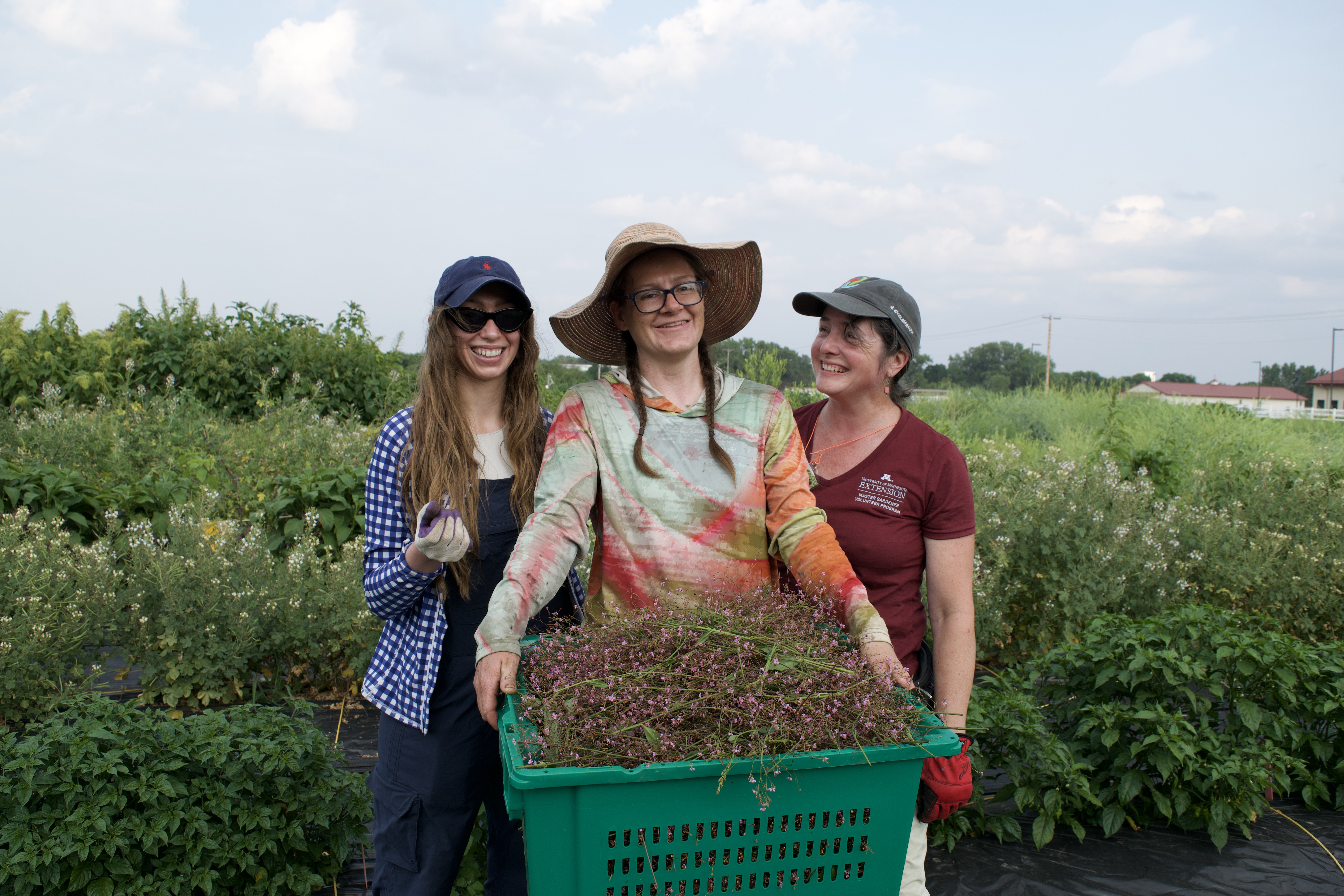 People smiling in field with produce bin